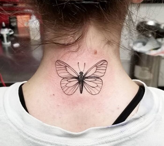 Black-and-white butterfly tattoo on the back of a neck, showcasing intricate wing details.