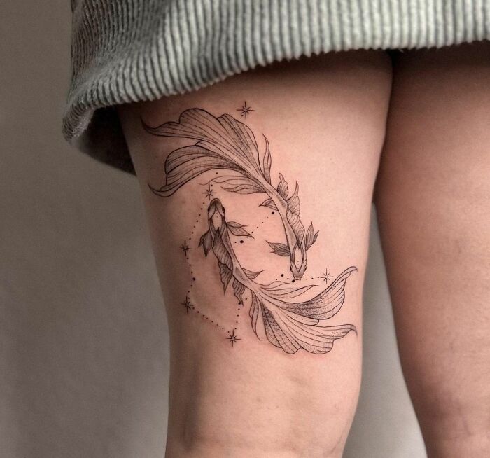 Pisces zodiac tattoo in black ink on thigh, featuring two elegant koi fish and stars.