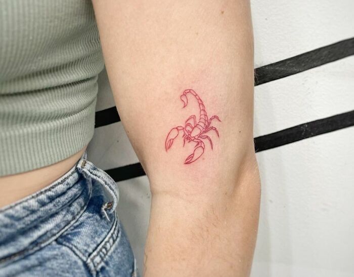 Zodiac tattoo of a red scorpion on a person's arm, representing Scorpio, in minimalistic style.