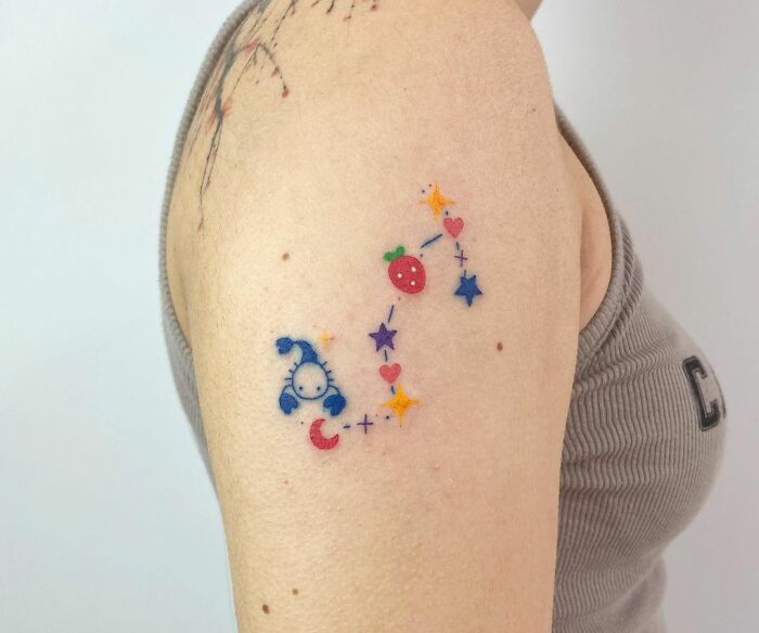Colorful zodiac tattoo on upper arm featuring stars, hearts, and constellation elements.
