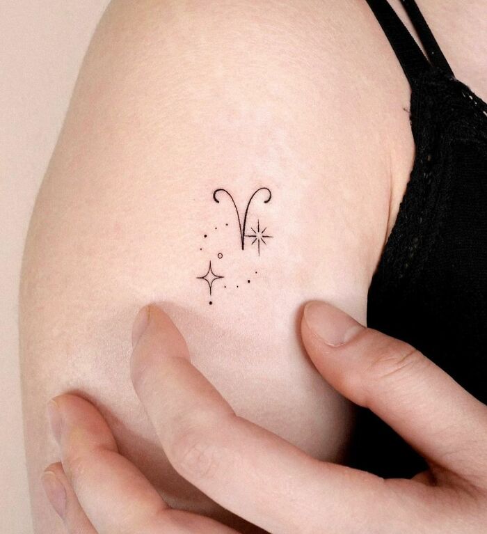 Minimalist zodiac tattoo on upper arm with dotted stars and Aries symbol.