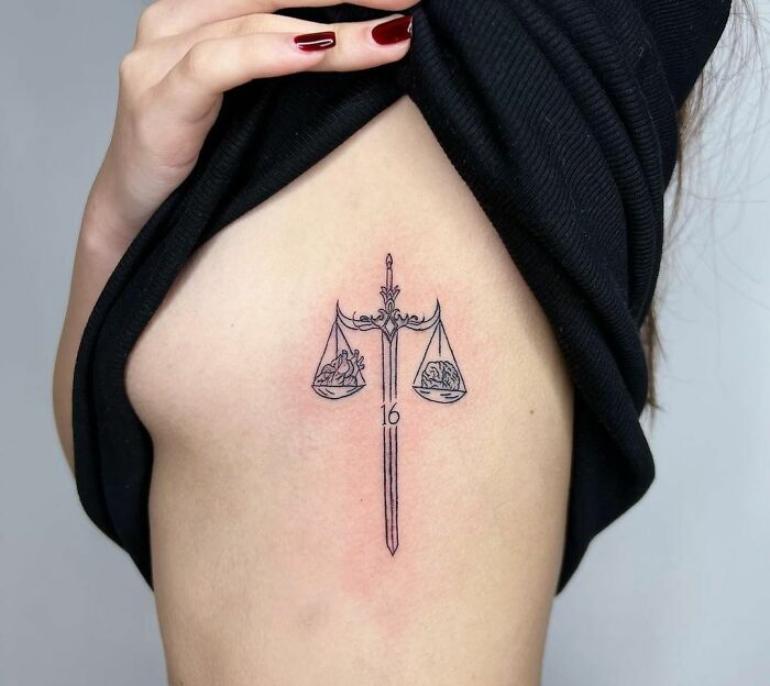 Zodiac tattoo of Libra scales on upper arm with intricate line design.