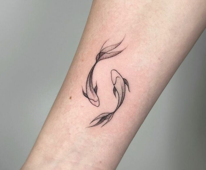Minimalist Pisces zodiac tattoo featuring two koi fish on forearm.