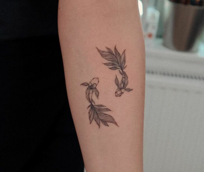 Minimalist Pisces zodiac tattoo featuring two stylized fish on a person's arm.