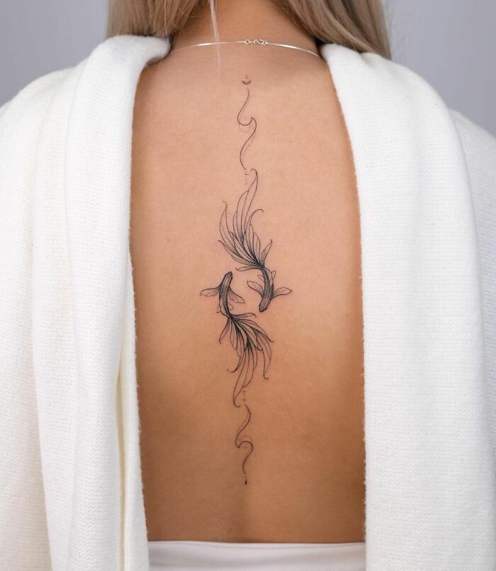 Zodiac tattoo of abstract Pisces fish on a woman's back, featuring delicate lines and flowing designs.