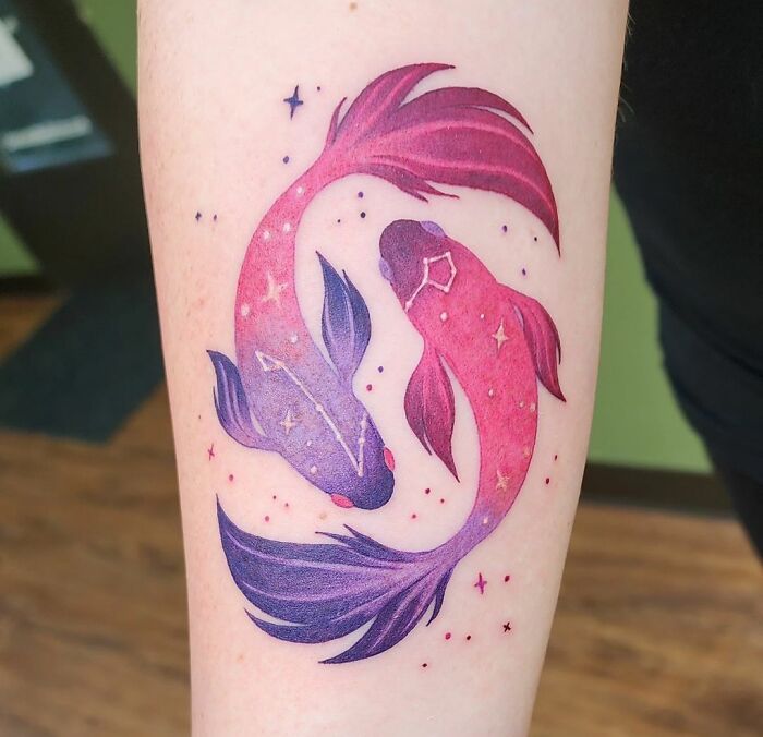 Colorful zodiac tattoo of two fish, representing Pisces, on forearm with stars and constellations.