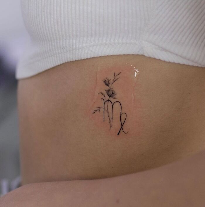 Zodiac tattoo of the Virgo symbol with floral design on a person's ribcage.