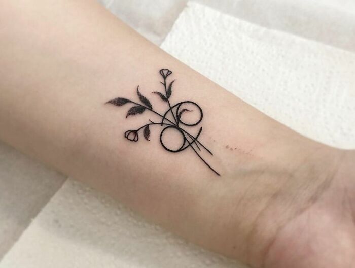Minimalist zodiac tattoo with floral elements on forearm, showcasing elegant black ink design.