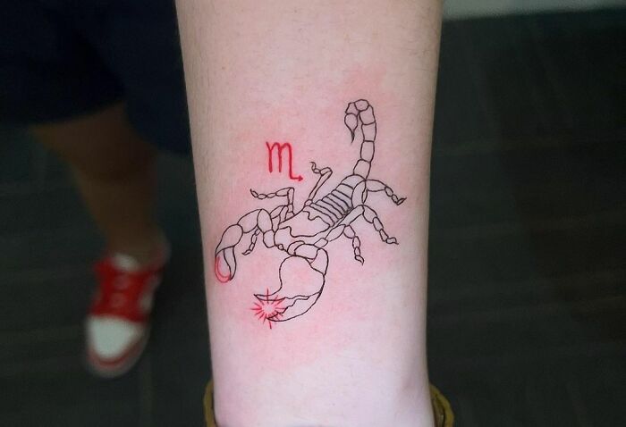 Scorpio zodiac tattoo in black and red ink on a forearm.