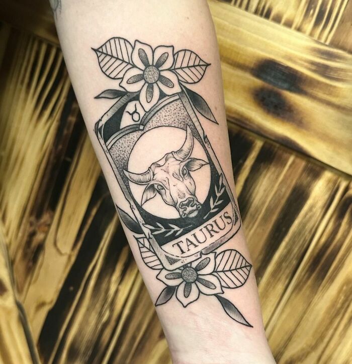 Taurus zodiac tattoo with bull and floral elements on forearm.