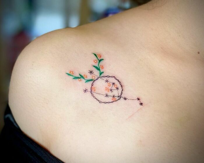 Minimalist zodiac tattoo with floral accents on shoulder, highlighting creative astrology-inspired design.