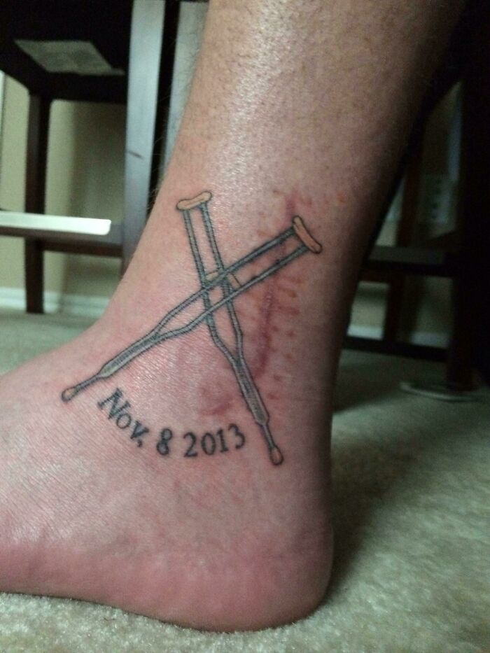 Ankle tattoo of crossed crutches with date Nov 8 2013 on the skin.