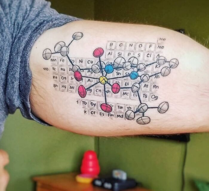 Science tattoo featuring a colorful molecular structure over a periodic table on an arm.