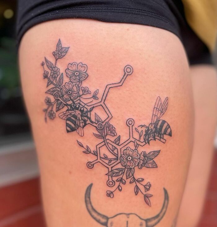 Science tattoo with floral and bee design on the thigh, featuring a chemical structure.