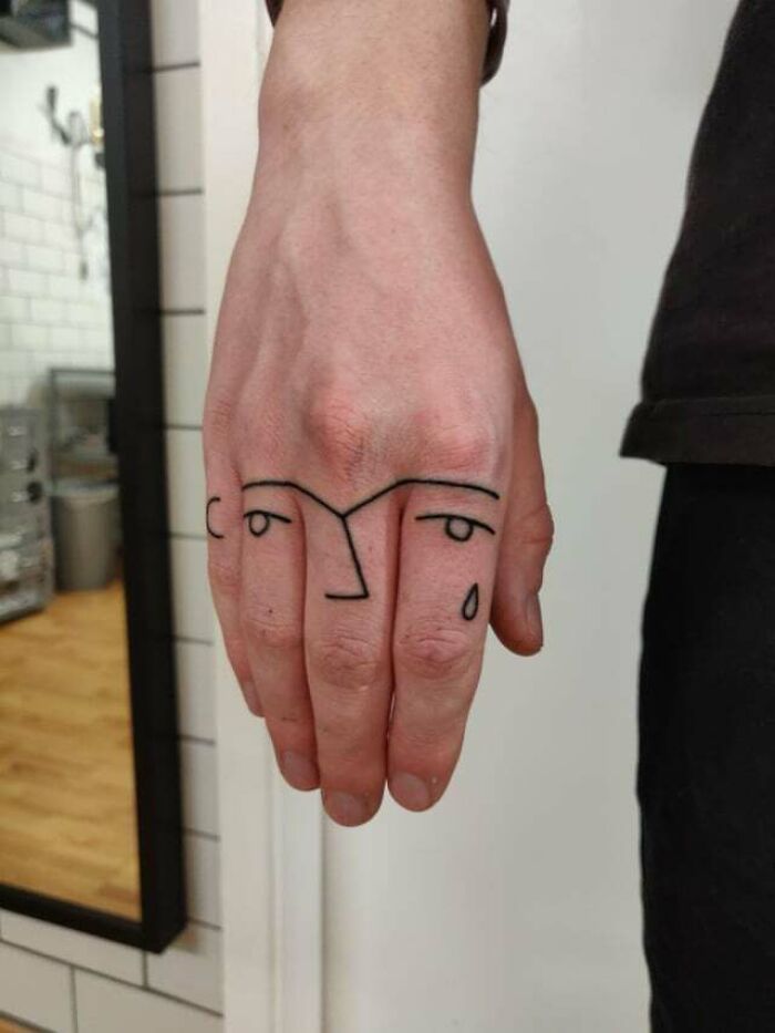 Abstract tattoo on hand featuring minimalist face design with black lines.
