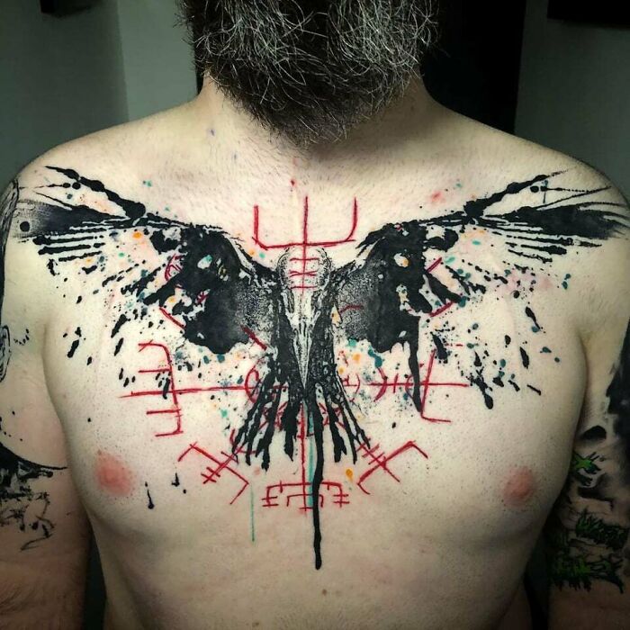 Abstract tattoo on a man's chest, featuring a stylized black and red bird design, showcasing self-expression and artistry.