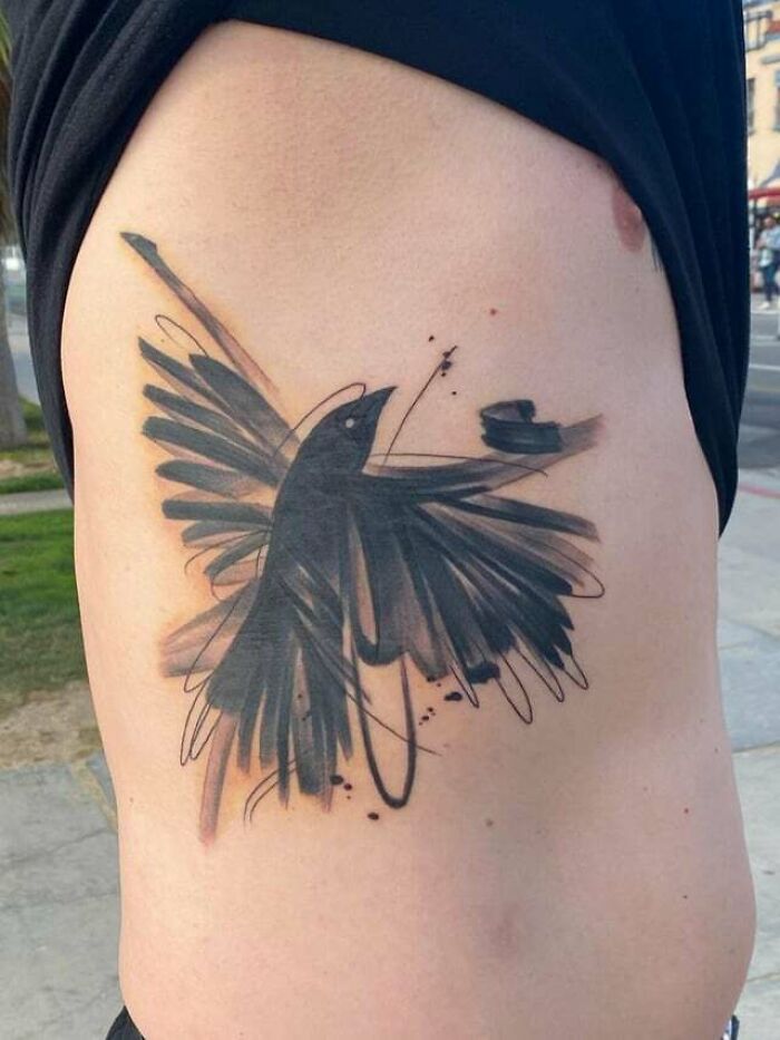 Abstract tattoo design of a stylized bird in black ink on a person's side, showcasing artistry and self-expression.
