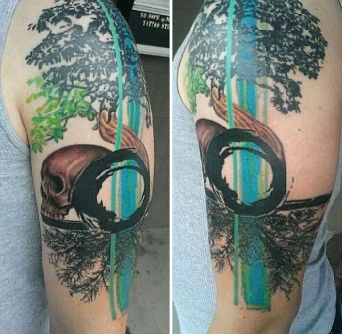 Abstract tattoo featuring a skull, trees, and bold geometric lines on an upper arm.