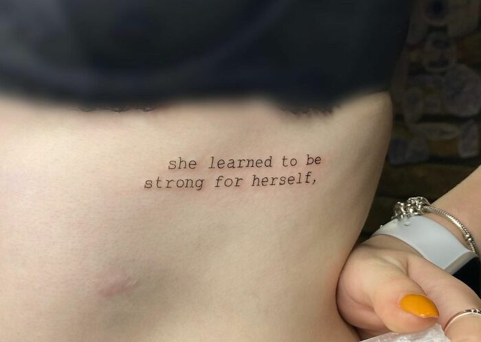 Tattoo with text "she learned to be strong for herself" on skin, symbolizing mental health and healing.