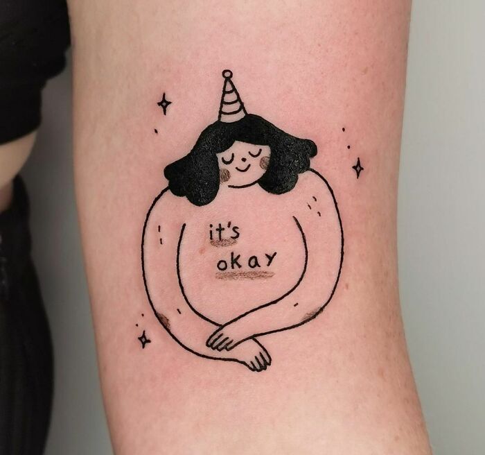 Illustration of a person with a party hat hugging themselves, featuring the words "it's okay," symbolizing mental health healing.