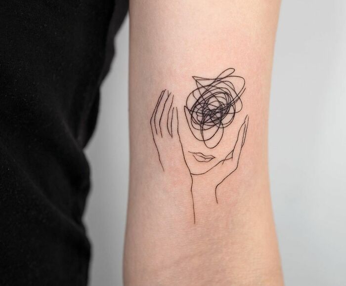 Minimalist mental health tattoo on arm, illustrating a face holding abstract thoughts above its head.