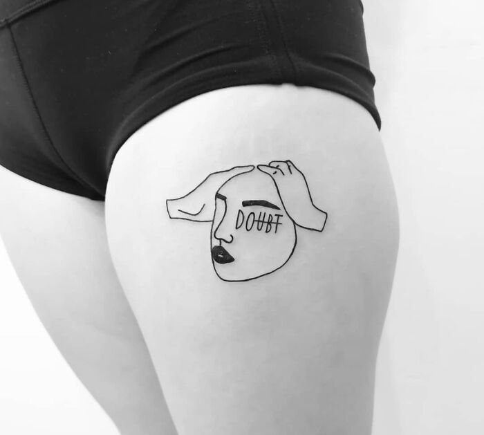 Minimalist mental health tattoo of a face with "doubt" on a thigh, symbolizing inner struggles and healing.