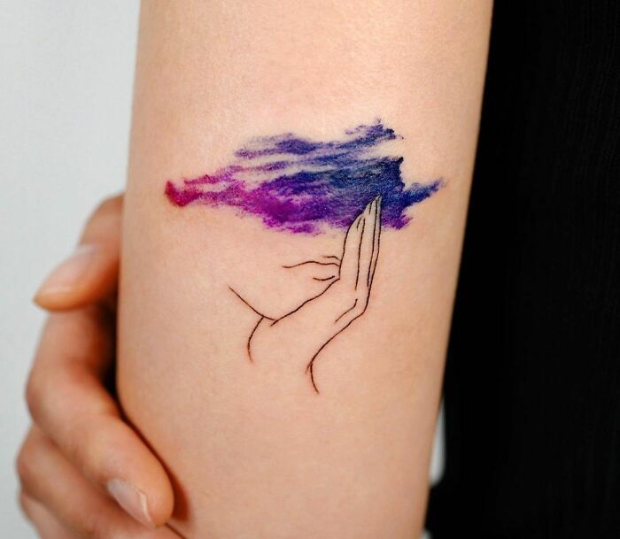 A watercolor tattoo on an arm, depicting a hand and a colorful cloud, symbolizing mental health and healing.