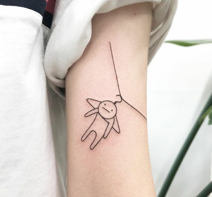 Minimalist mental health tattoo featuring a simple figure hanging from a line, symbolizing healing and resilience.