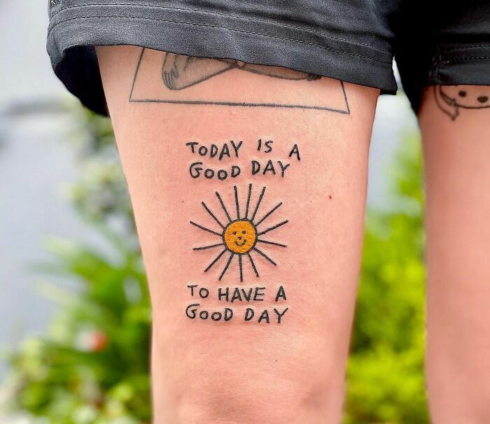 Mental health tattoo on a thigh featuring a smiling sun and the phrase "Today is a good day to have a good day."