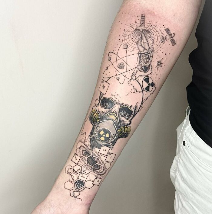 Science tattoo on forearm featuring astronaut, atom, and skull with gas mask, representing scientific elements and exploration.