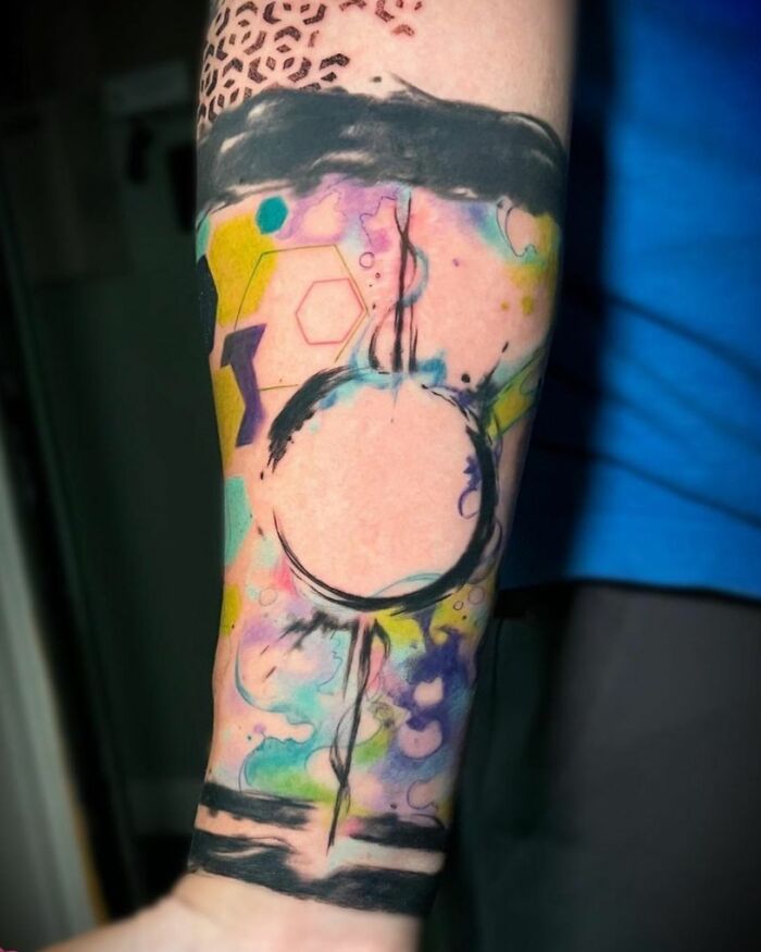 Abstract tattoo design with colorful geometric shapes and watercolor effects on a person's arm.