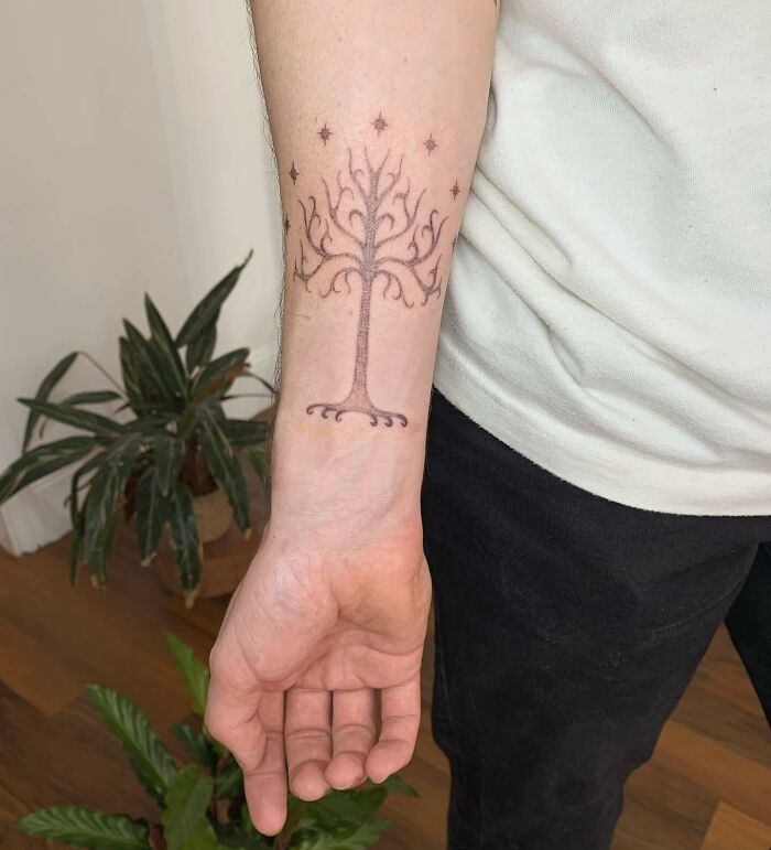 "White Tree tattoo on forearm, inspired by Lord of the Rings, with surrounding stars, set in a casual indoor setting."