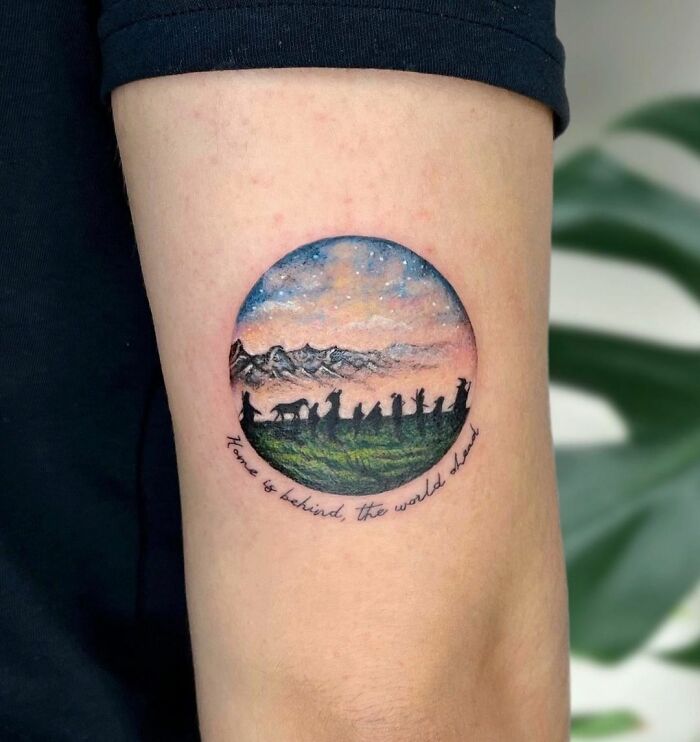 Tattoo of the Fellowship from Lord of the Rings with mountains and sky in a circular design.