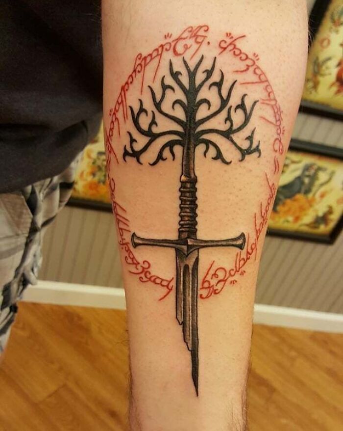Tattoo of the White Tree and sword with Elvish script, inspired by Lord of the Rings, on a person's forearm.