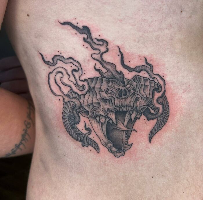 Detailed black and grey Lord of the Rings tattoo of a roaring dragon on a person's side.