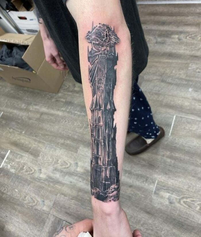 Forearm tattoo of a Lord of the Rings tower in black ink, detailed design with the Eye of Sauron.