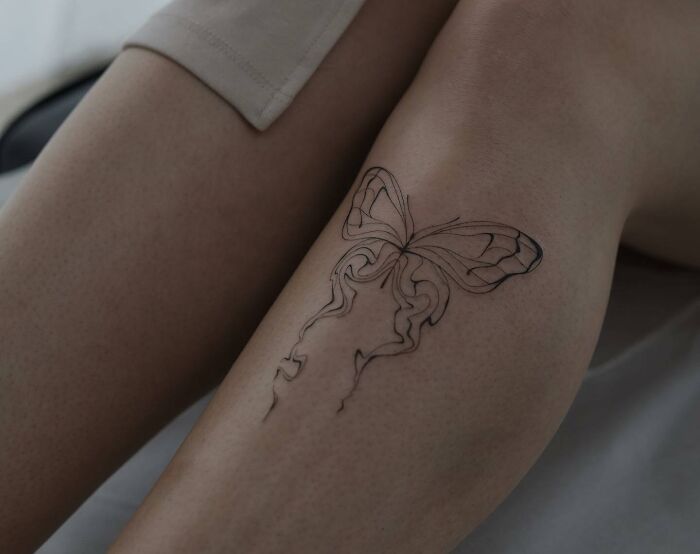 Line art butterfly tattoo on a person's leg, showcasing elegant and creative design.