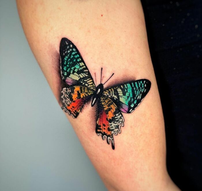 Colorful butterfly tattoo on arm, showcasing vibrant patterns and realistic detail.
