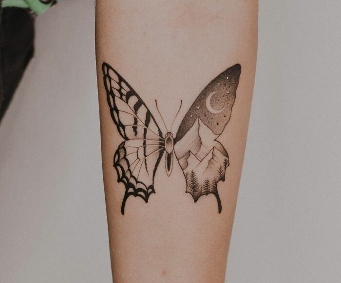 Butterfly tattoo with intricate black and white design featuring a mountain and forest scene on one wing.