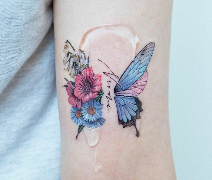 Colorful butterfly tattoo with blue and pink wings, accented by vibrant flowers on the forearm.