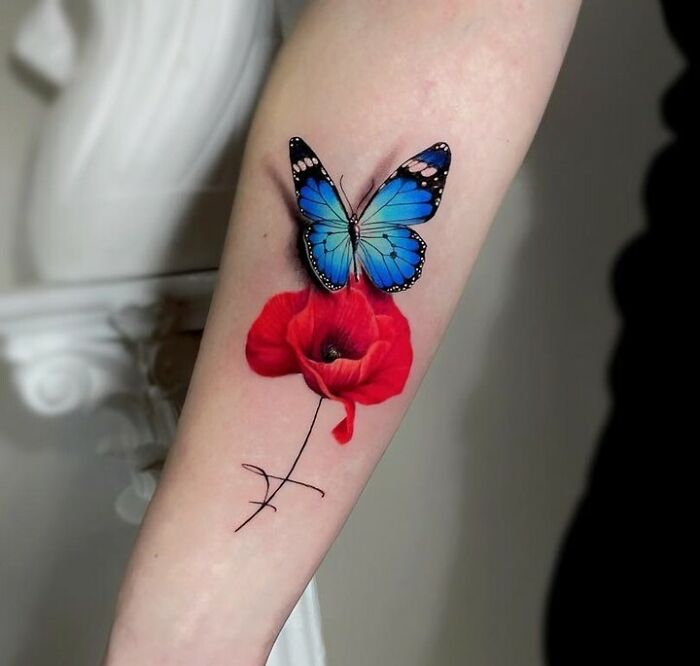 A colorful butterfly tattoo with blue wings and a red flower on an arm.