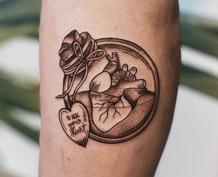 Heart-themed mental health tattoo with a healing message on a person's arm.