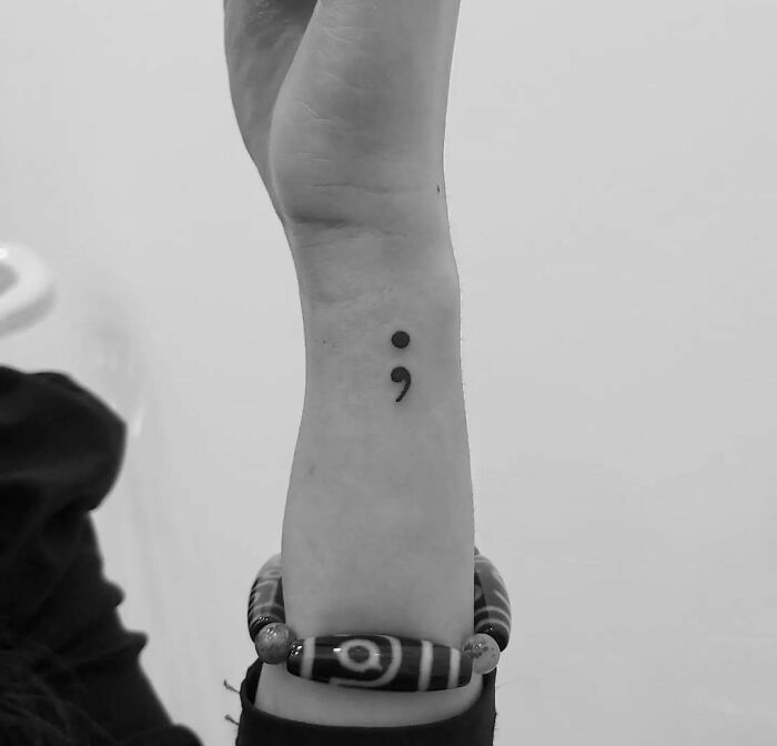 Semicolon tattoo on a wrist symbolizing mental health healing, with a patterned bracelet.