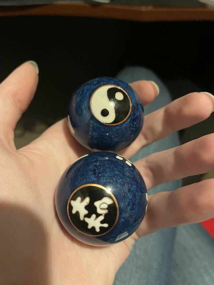 Hand holding two mysterious blue Baoding balls with yin-yang and Chinese character symbols, curious objects discovered.