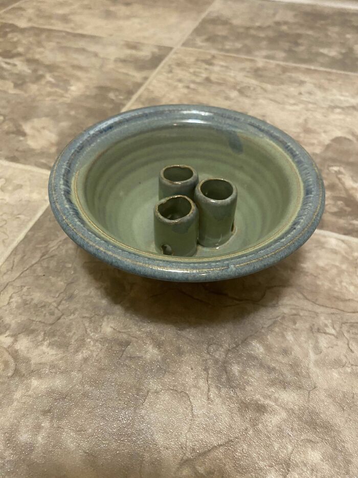 Ceramic bowl with three hollow cylindrical protrusions seen as a mysterious object found unexpectedly on a tiled floor.