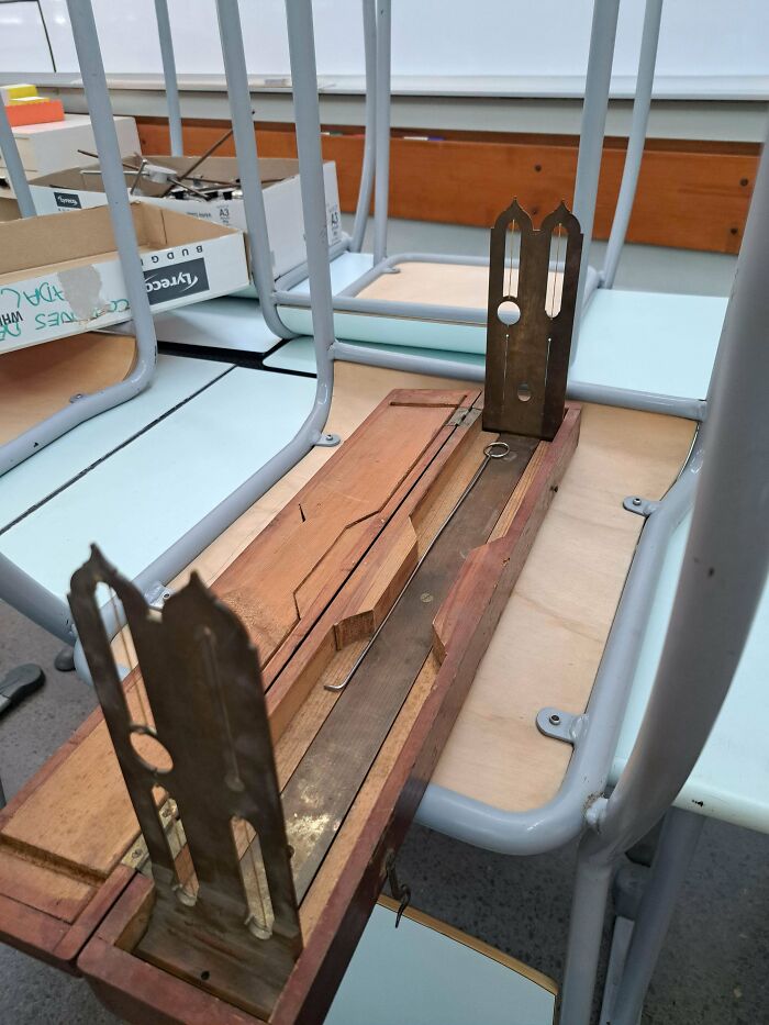 Wooden box with metal components inside a classroom setting, a mysterious object people stumbled upon and examined closely.