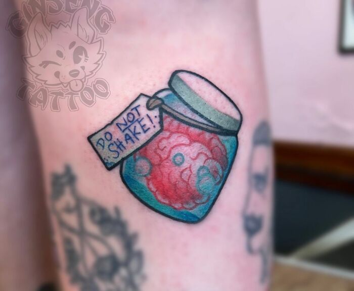 Tattoo of a brain in a jar with a "Do Not Shake" tag, symbolizing mental health awareness.