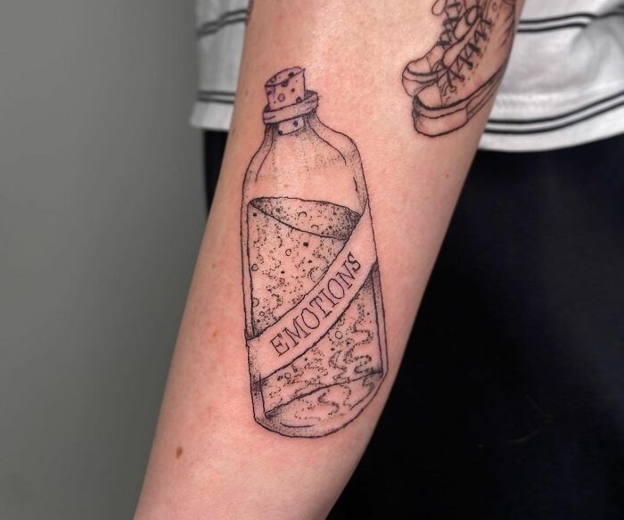 Tattoo of a glass bottle labeled "Emotions" on an arm, symbolizing mental health and healing through art.
