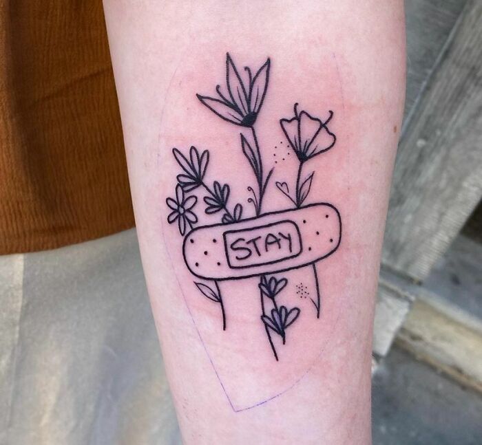 Floral tattoo with band-aid labeled "Stay," symbolizing mental health and healing.