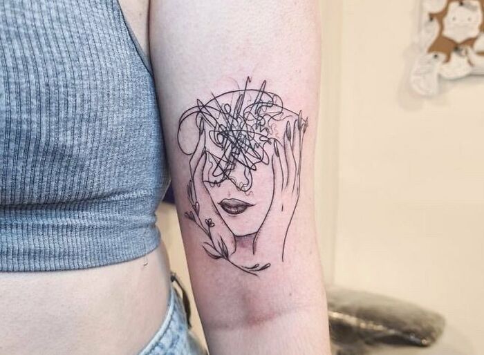 Minimalist mental health tattoo on arm, featuring a face with scribbled lines suggesting emotional turmoil.